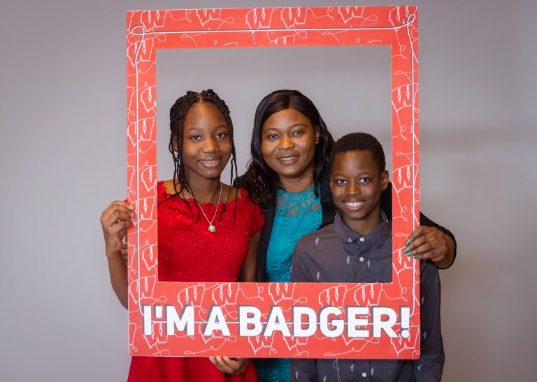 Returning adult student with her family looking through a frame that says, "I'm a badger."